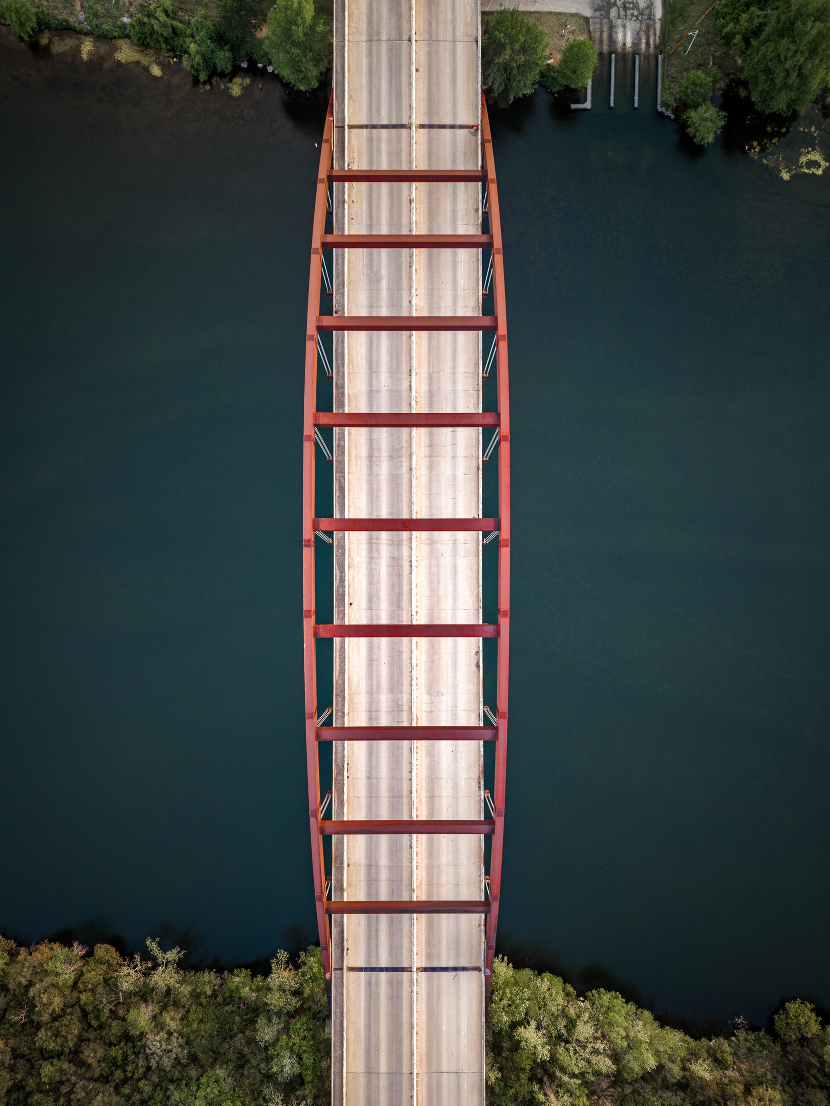 Suspended: aerial view looking straight down on the red steel arch of the Pennybacker (360) Bridge over Lake Austin