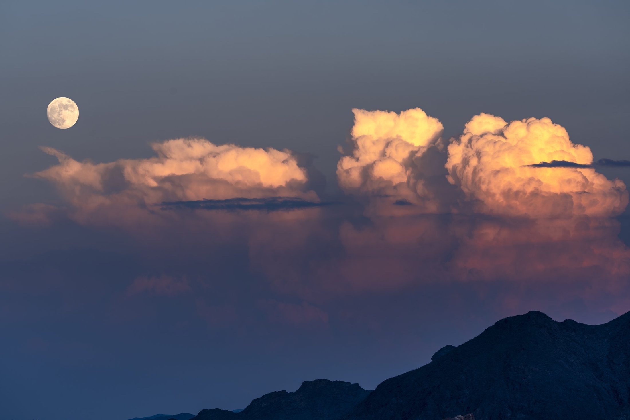 A full moon beside golden storm clouds over the mountains of Big Bend National Park